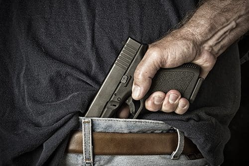 close up shot of a man grasping the handle of a pistol in his waistband