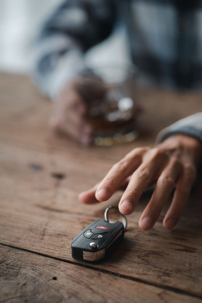 Close up of a hand reaching for car keys of a man holding a glass of brandy blurred in the background